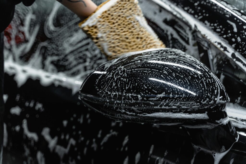 pexels photo 6872146 6872146 1 Hand scrubbing a car mirror with a sponge covered in soap at a car wash.