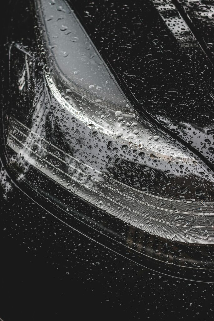 Close-up of a car headlight covered with raindrops, showcasing sleek design and weather details.